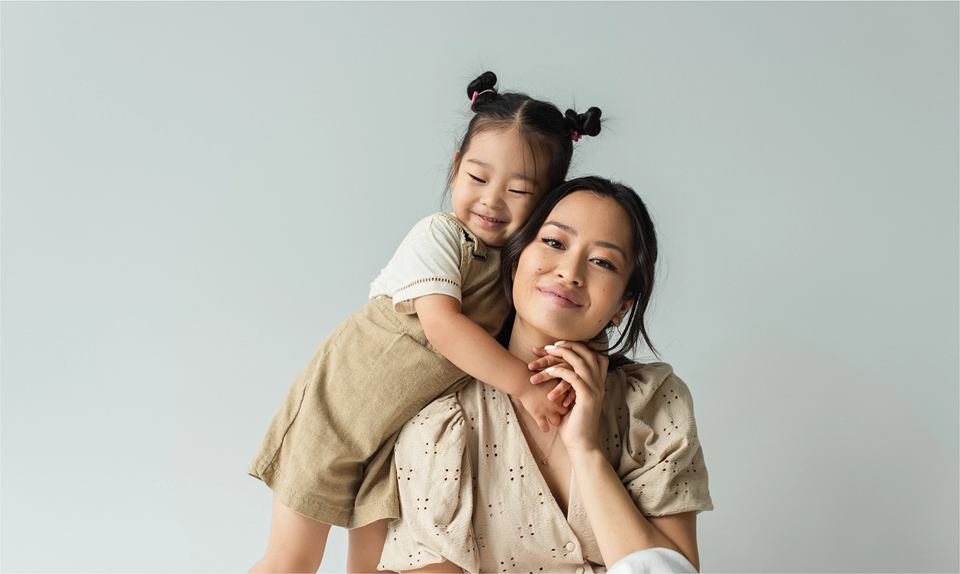 A woman holds a young child's hand. The child is on woman's back and has her arms around the woman's neck.